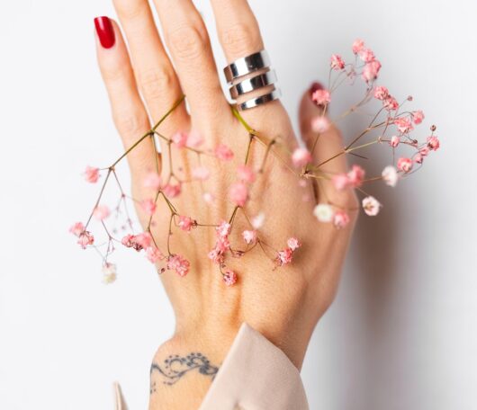 soft-gentle-photo-woman-hand-with-big-ring-red-manicure-hold-cute-little-pink-dried-flowers-white